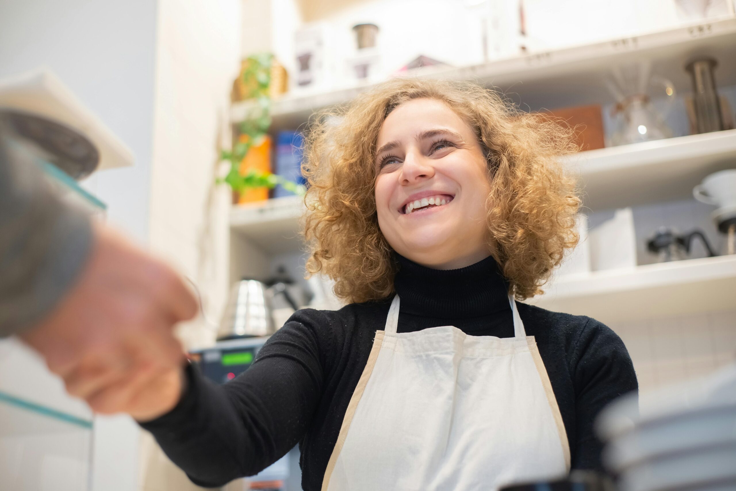 Smiling barista in caf&eacute;, engaging positively with customer, signifying hospitality.